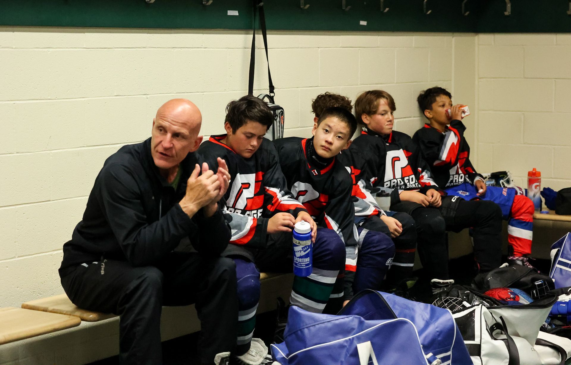 Youth hockey team and coach sitting on a bench in the locker room, drinking water during a break.