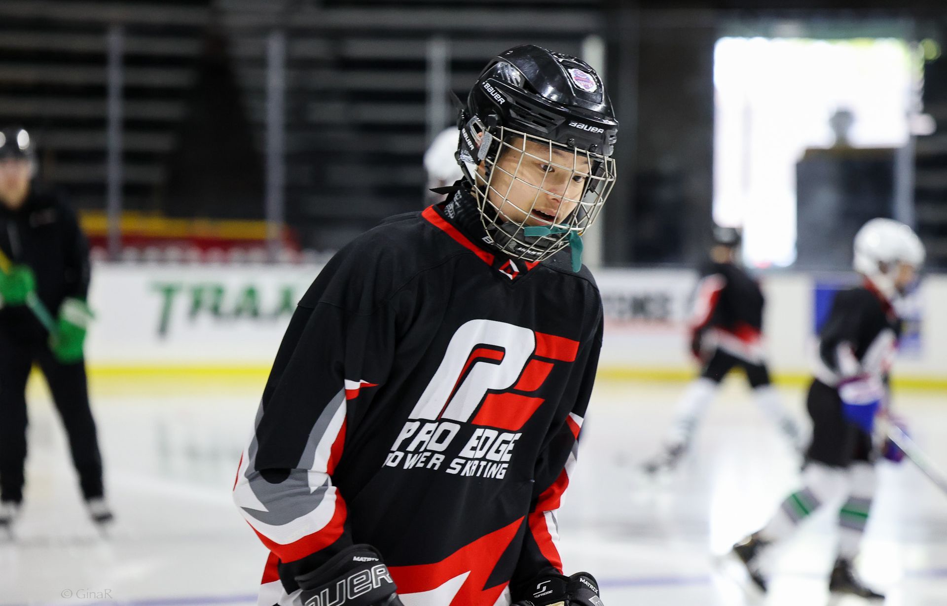 Young hockey player in black and red jersey skating on an indoor ice rink