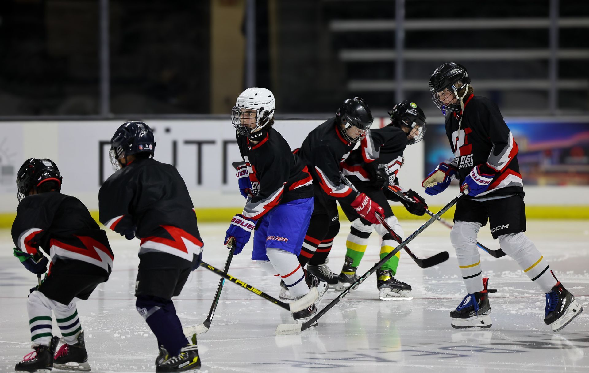 Youth ice hockey players in black and white uniforms skating and battling for the puck on the rink