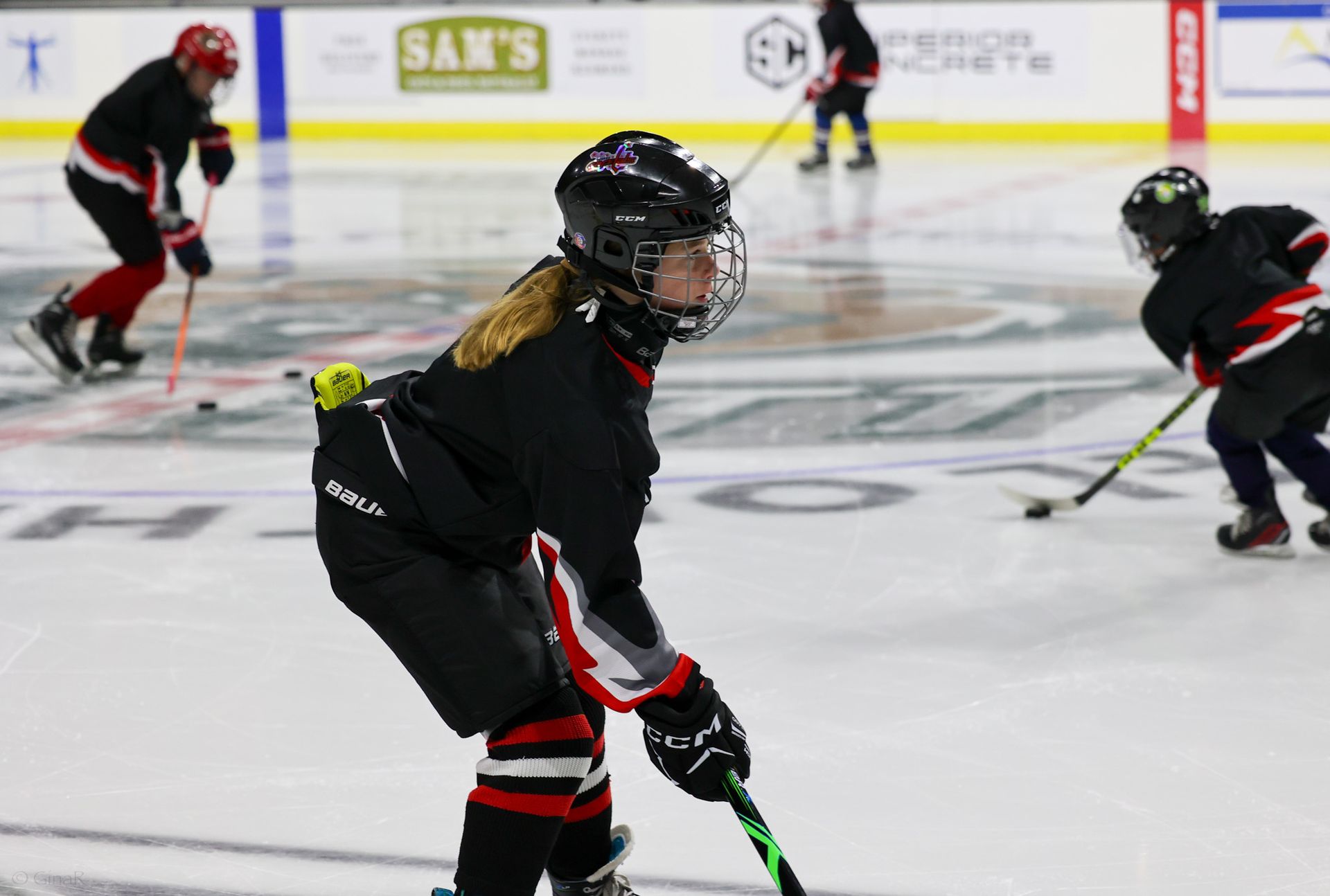 Youth hockey players in black and red skating on an ice rink during practice