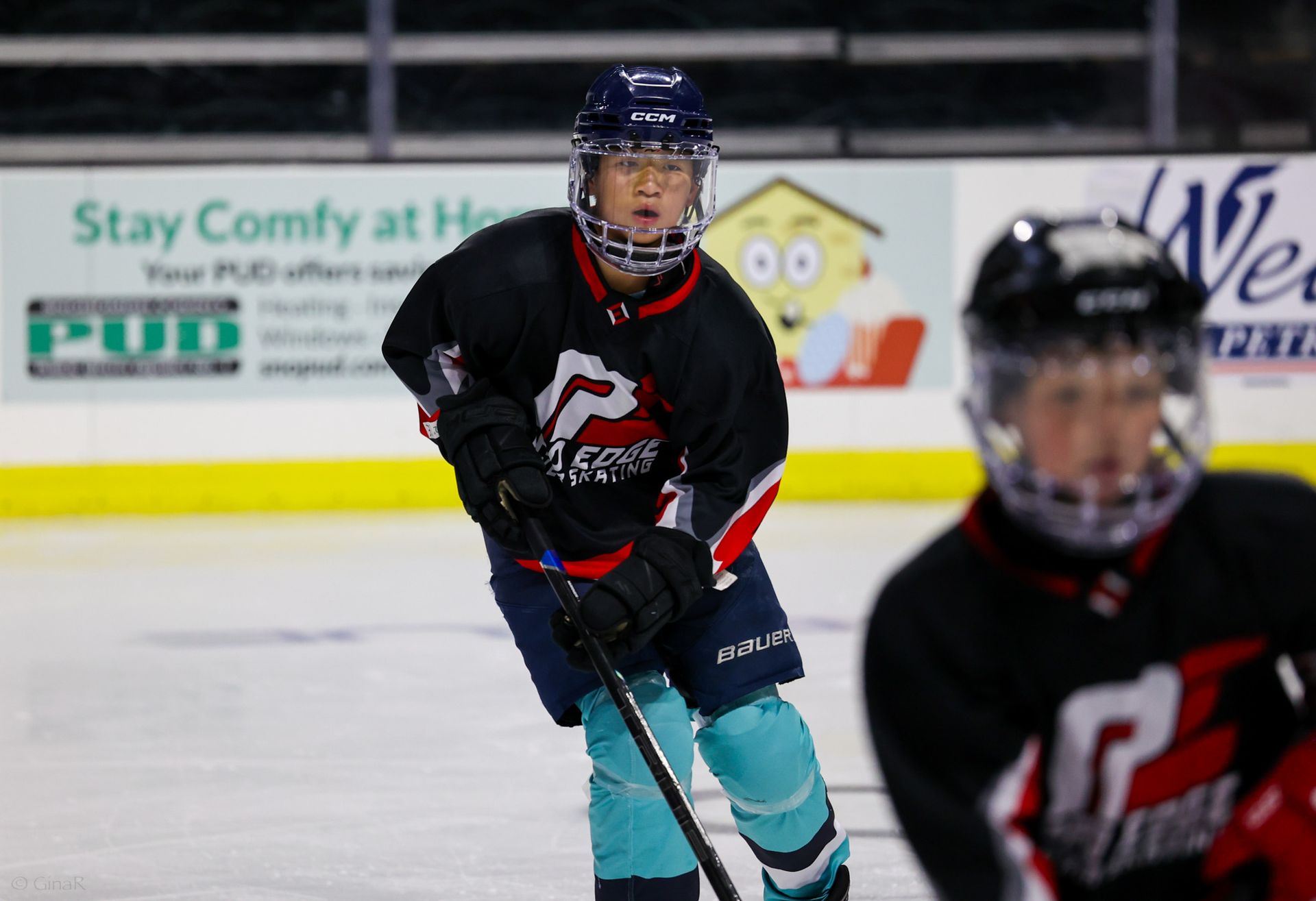 Ice hockey players in black and teal uniforms skate on an indoor rink during play