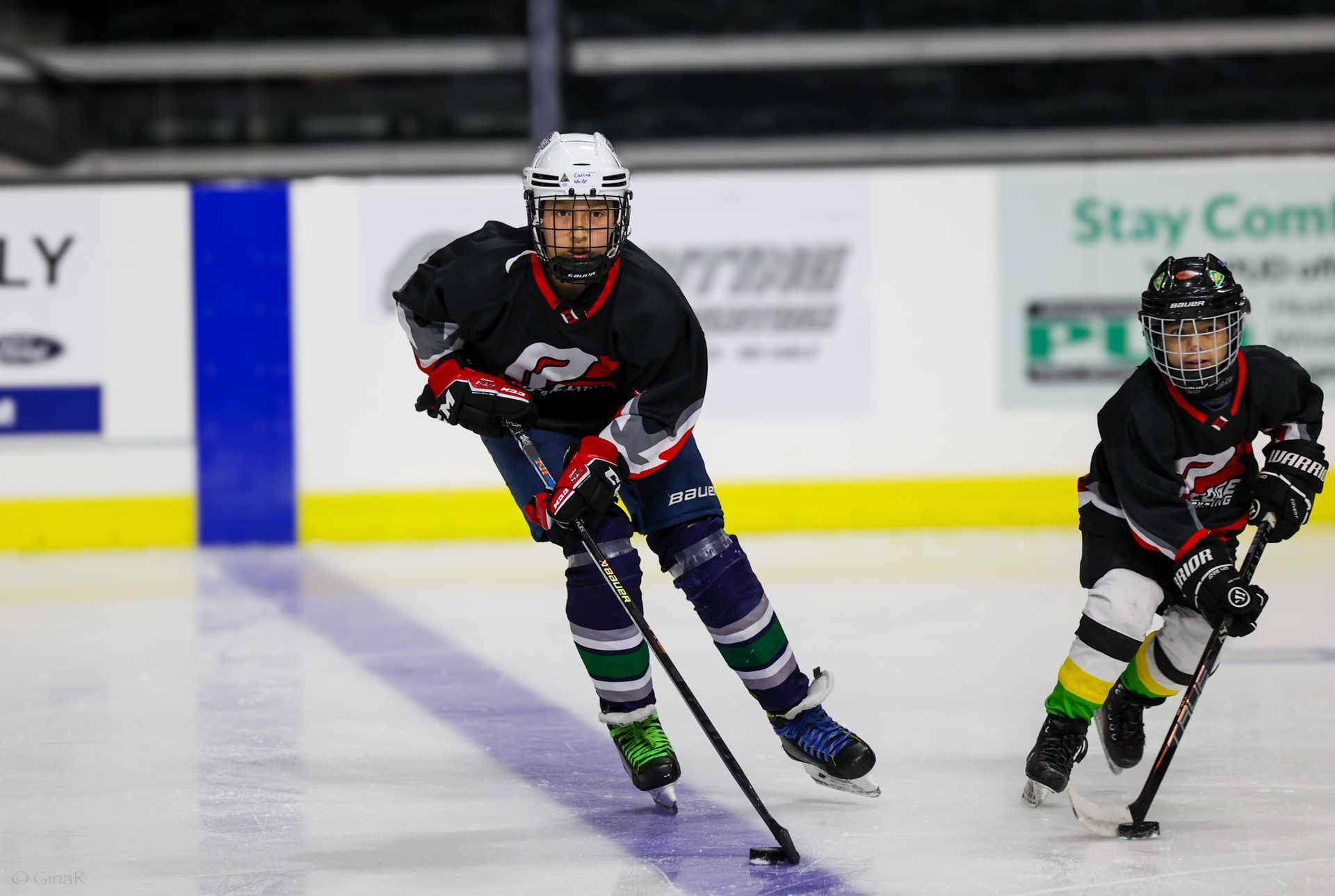 Two youth hockey players in black jerseys skating on an indoor ice rink