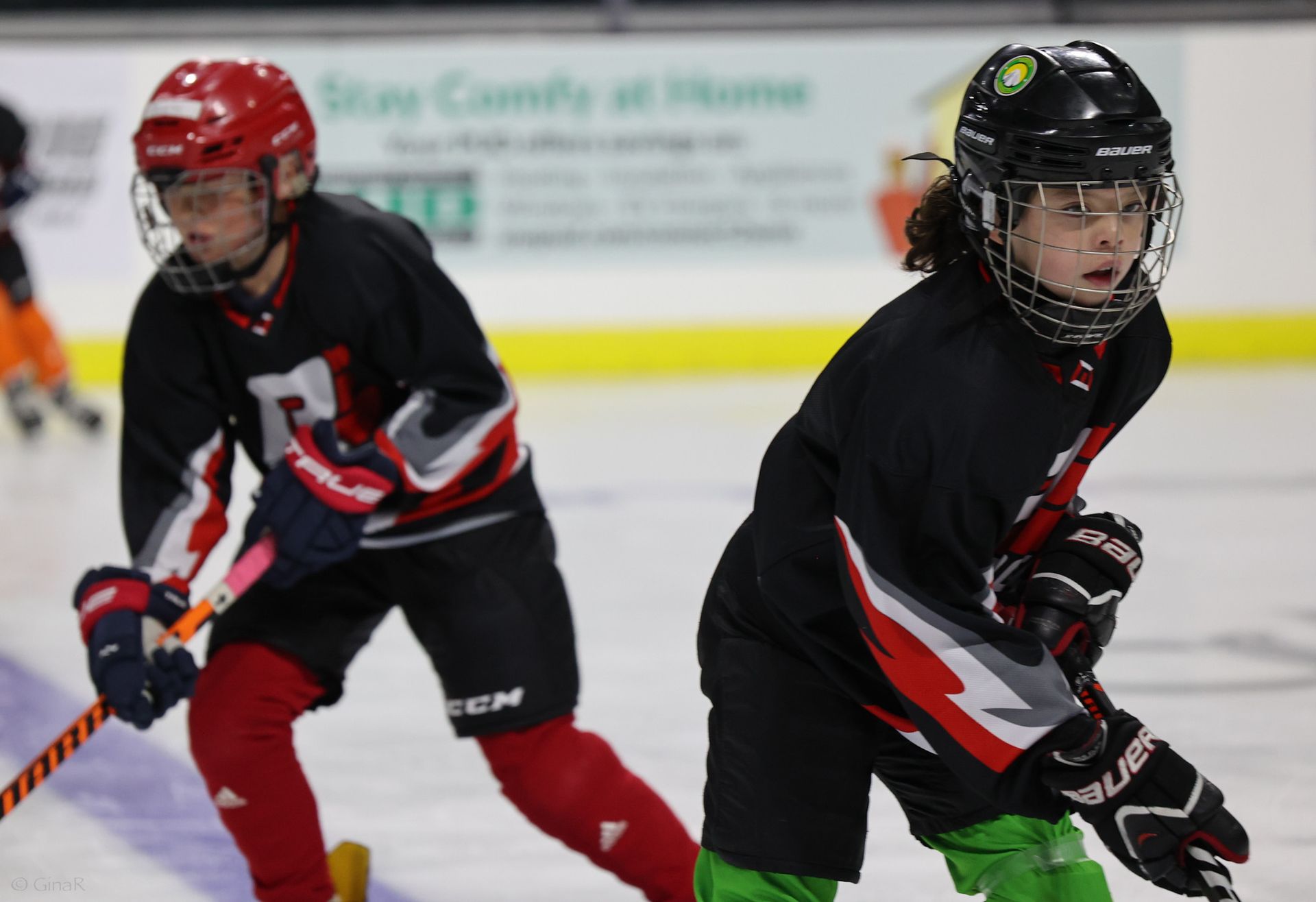 Two hockey players in black and red uniforms skating on an ice rink