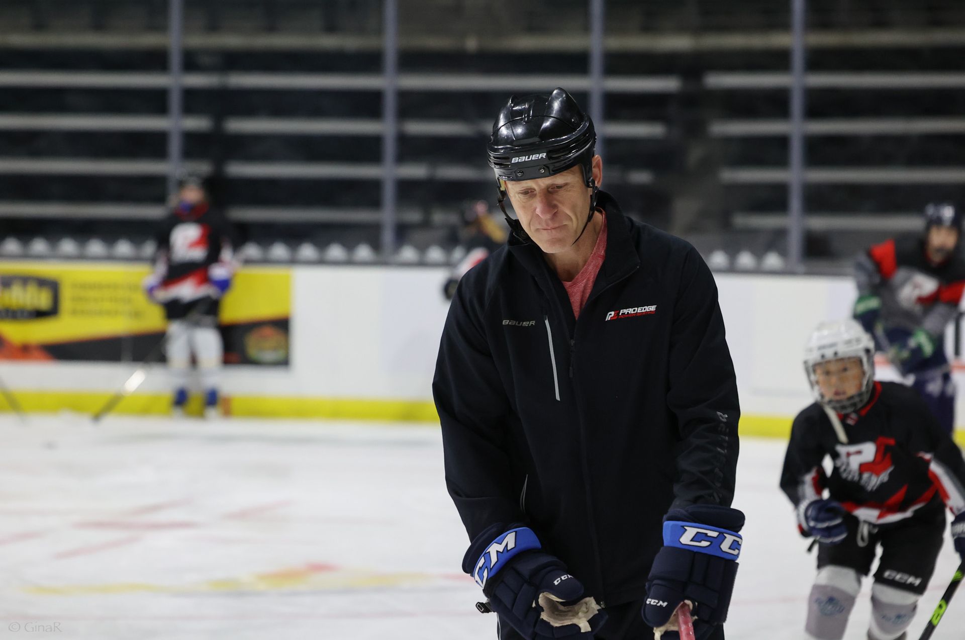 Ice hockey players in black and red gear on an indoor rink, with one player in focus in the foreground.