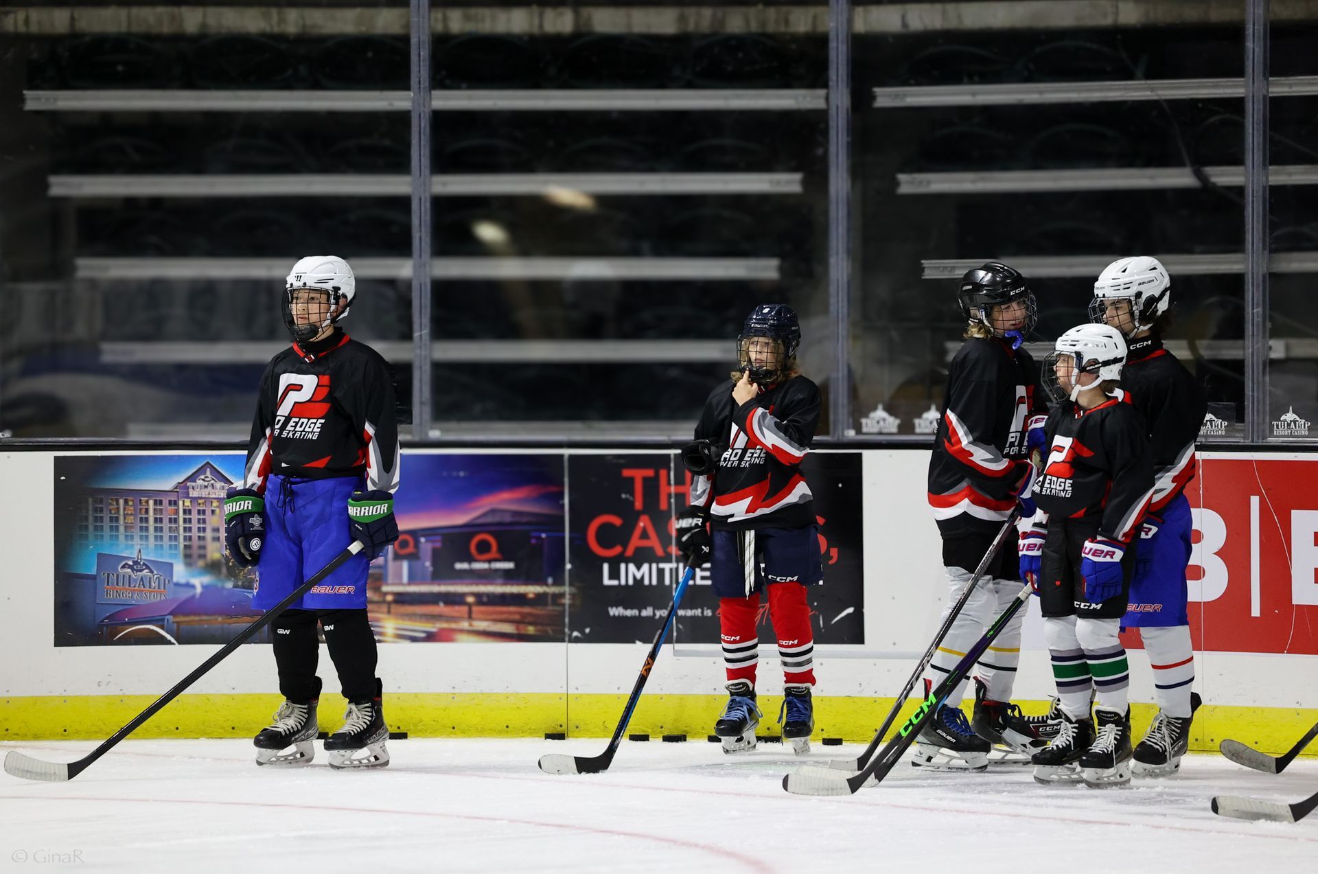 Youth ice hockey players in black uniforms stand on the rink during a break in play.