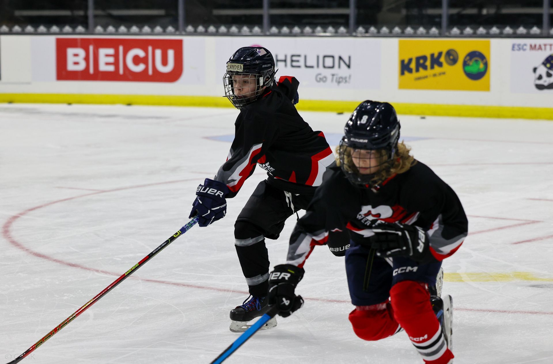 Two hockey players in black and red gear racing on the ice