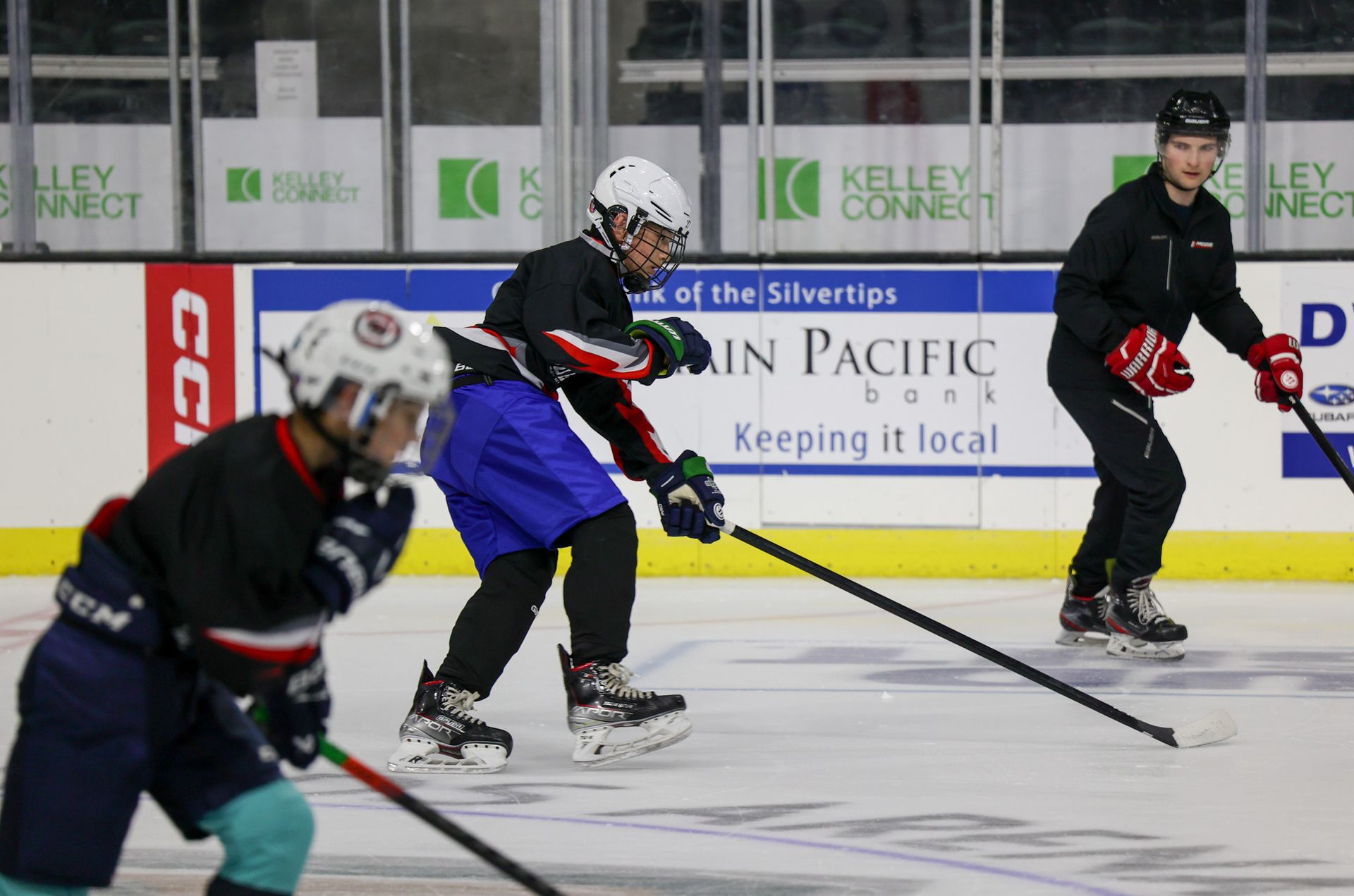 Ice hockey players in dark jerseys skate during a game on an indoor rink.