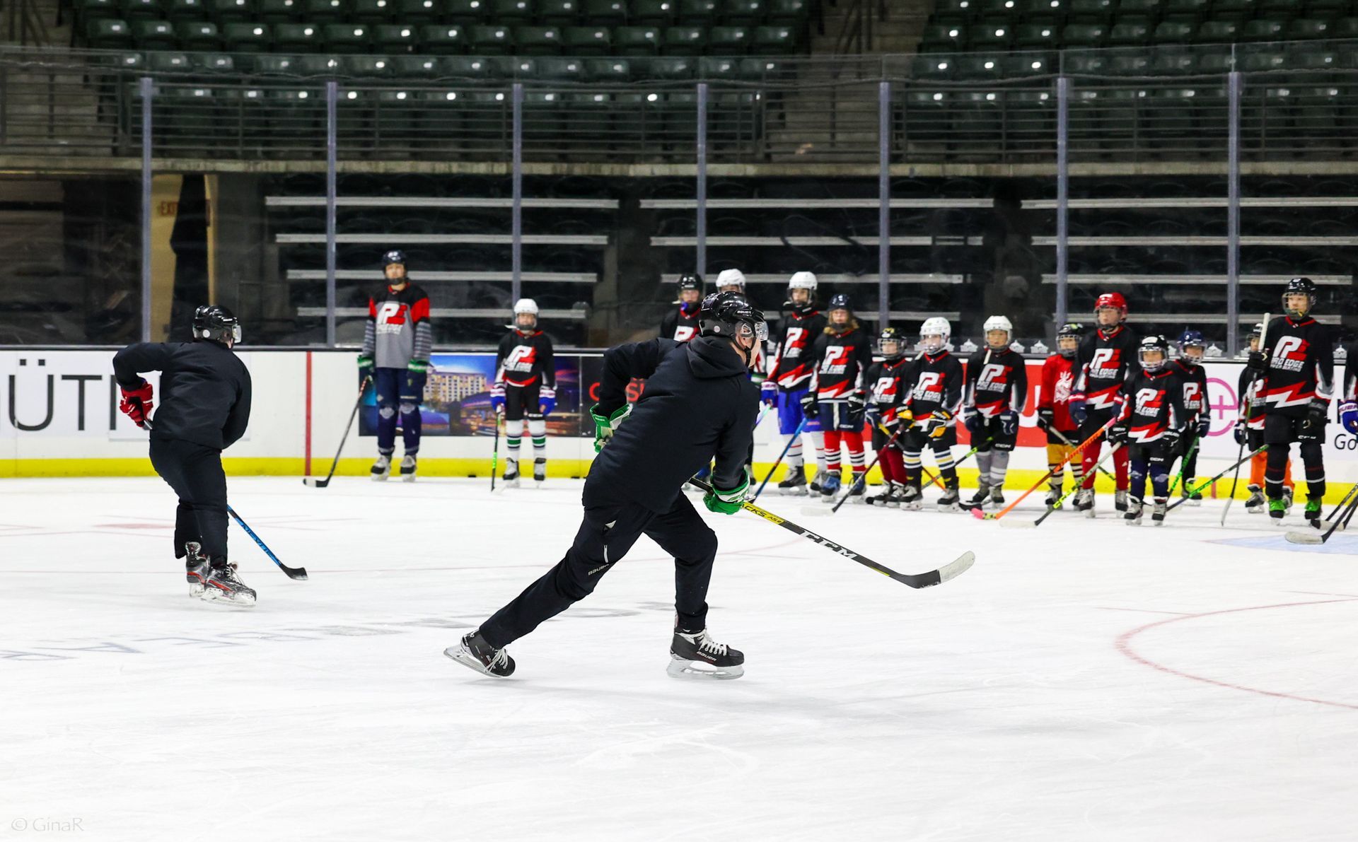 Ice rink practice with two skaters on the ice and a hockey team lined up on the bench in the background