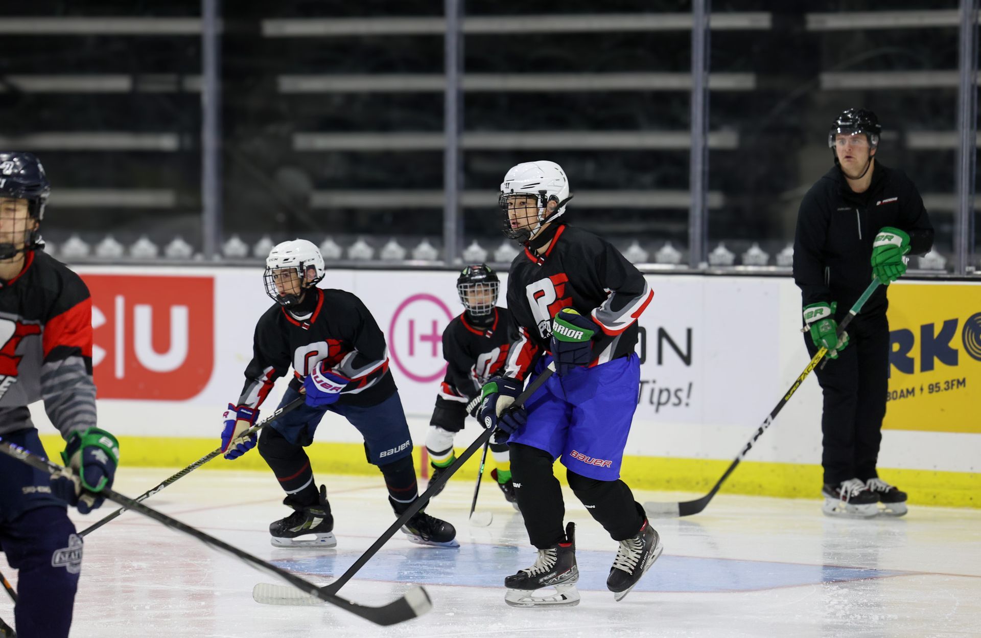 Youth ice hockey players in black and blue uniforms skating on an indoor rink during a game