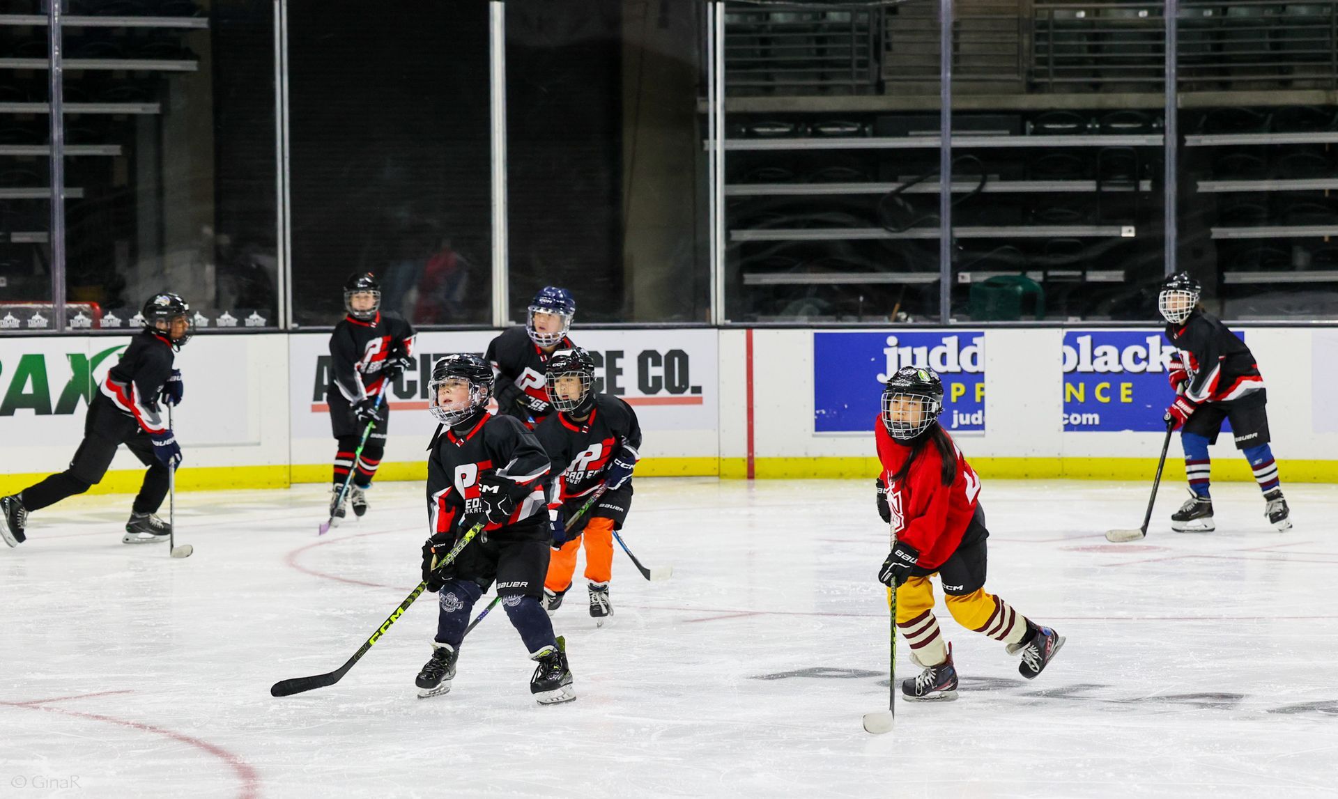 Hockey players in black and red uniforms skate on an indoor rink during a game.
