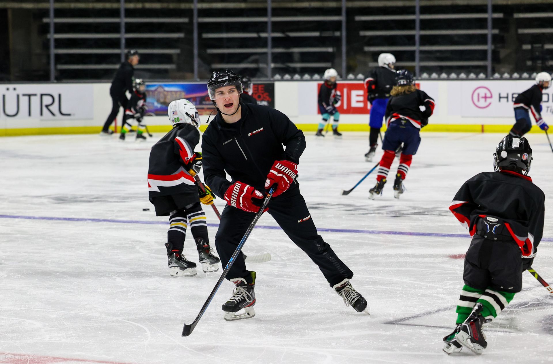 Hockey players in black and red skating on ice during a game, with one player centered holding a stick.