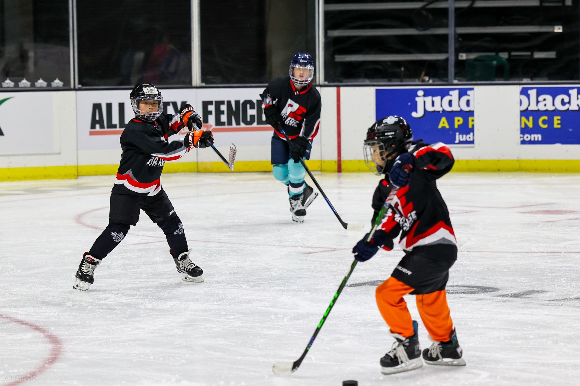 Ice hockey players in black and red uniforms on an indoor rink, one handling the puck.
