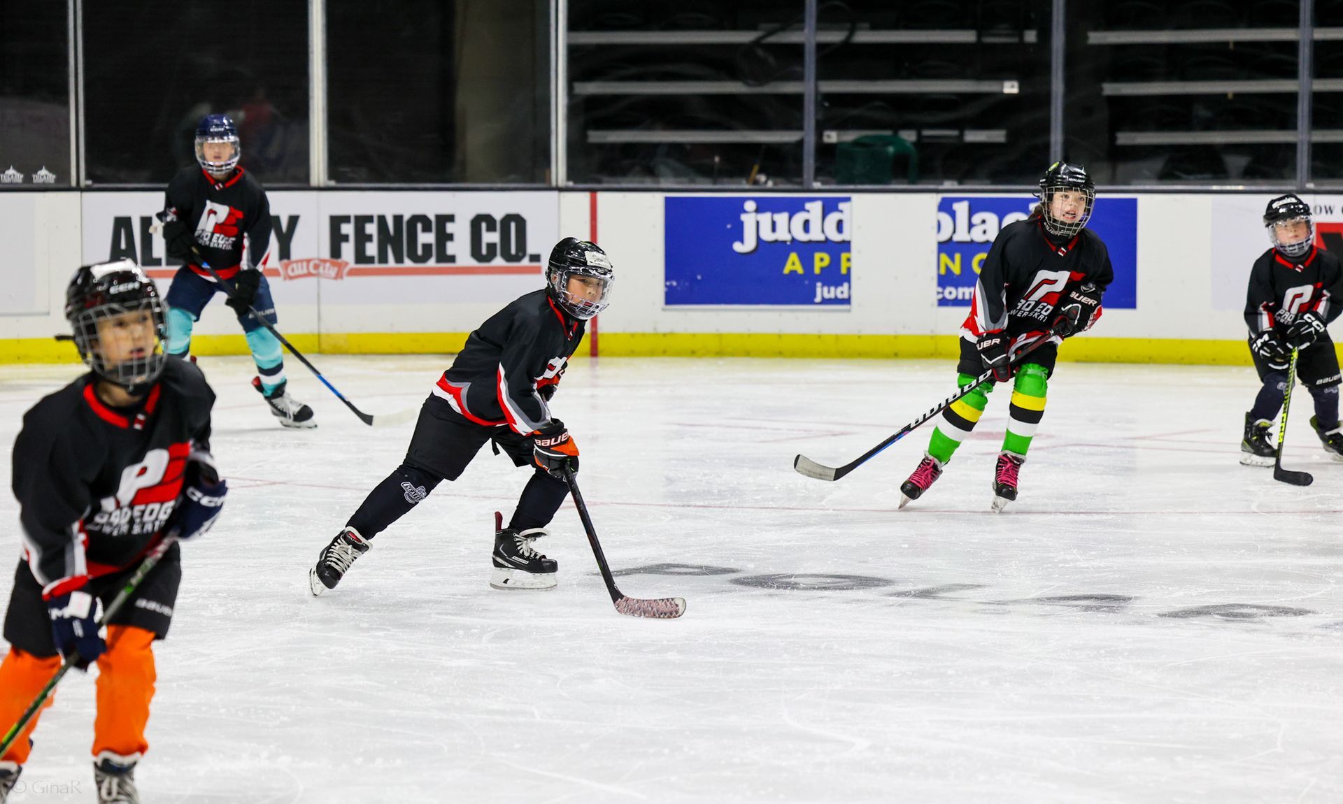 Youth hockey players skating during an indoor game on an ice rink, one in neon green socks.