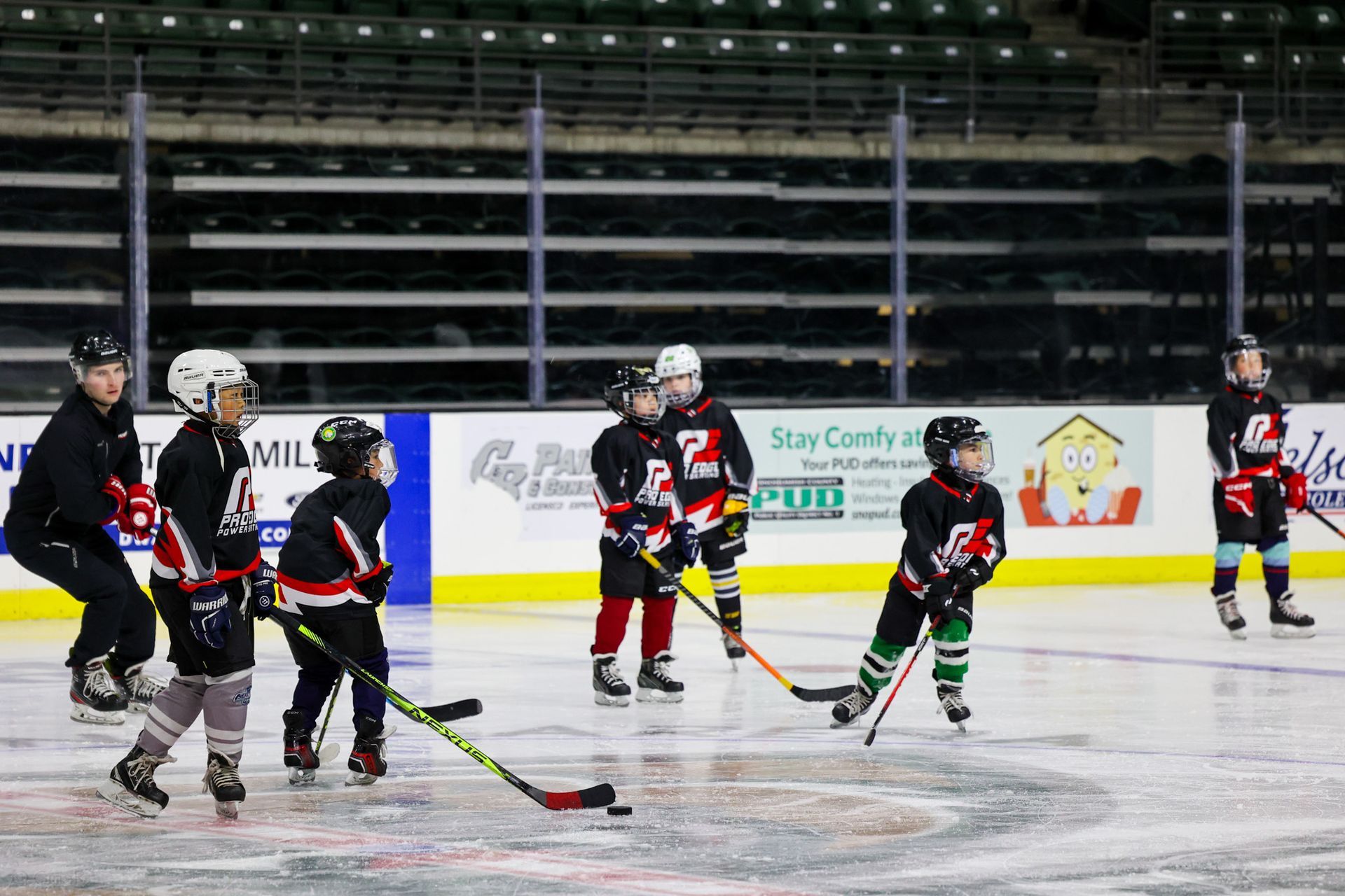 Youth hockey players on ice during practice, wearing black and red uniforms.