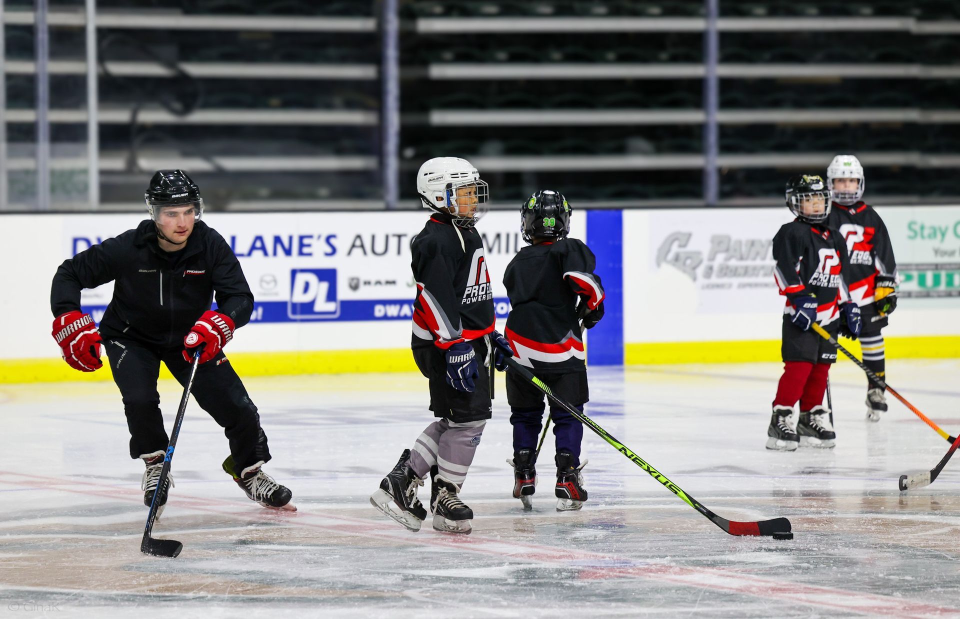 Inline hockey players in black and red uniforms skating on an indoor rink during a game