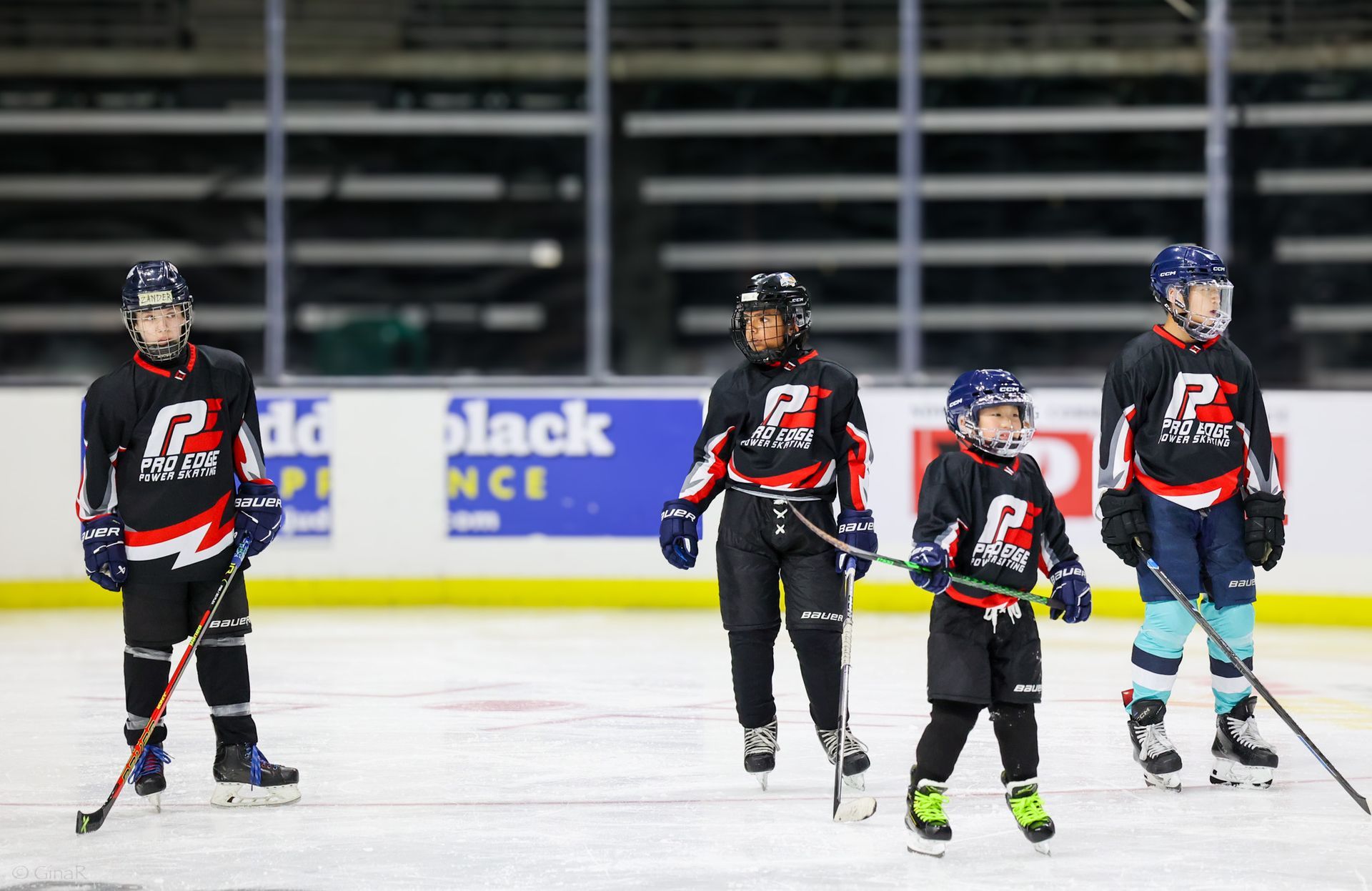 Four hockey players in black jerseys standing on an ice rink during practice