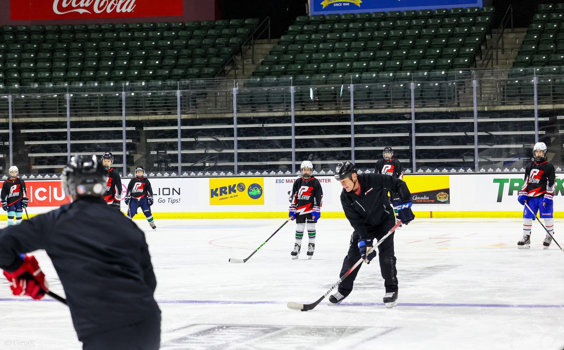 Ice hockey practice on an indoor rink, with players skating and handling sticks near the goal.