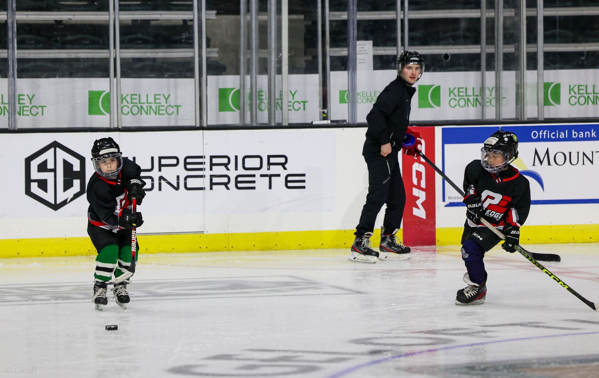 Youth hockey players on ice during a game, with a coach and boards in the background