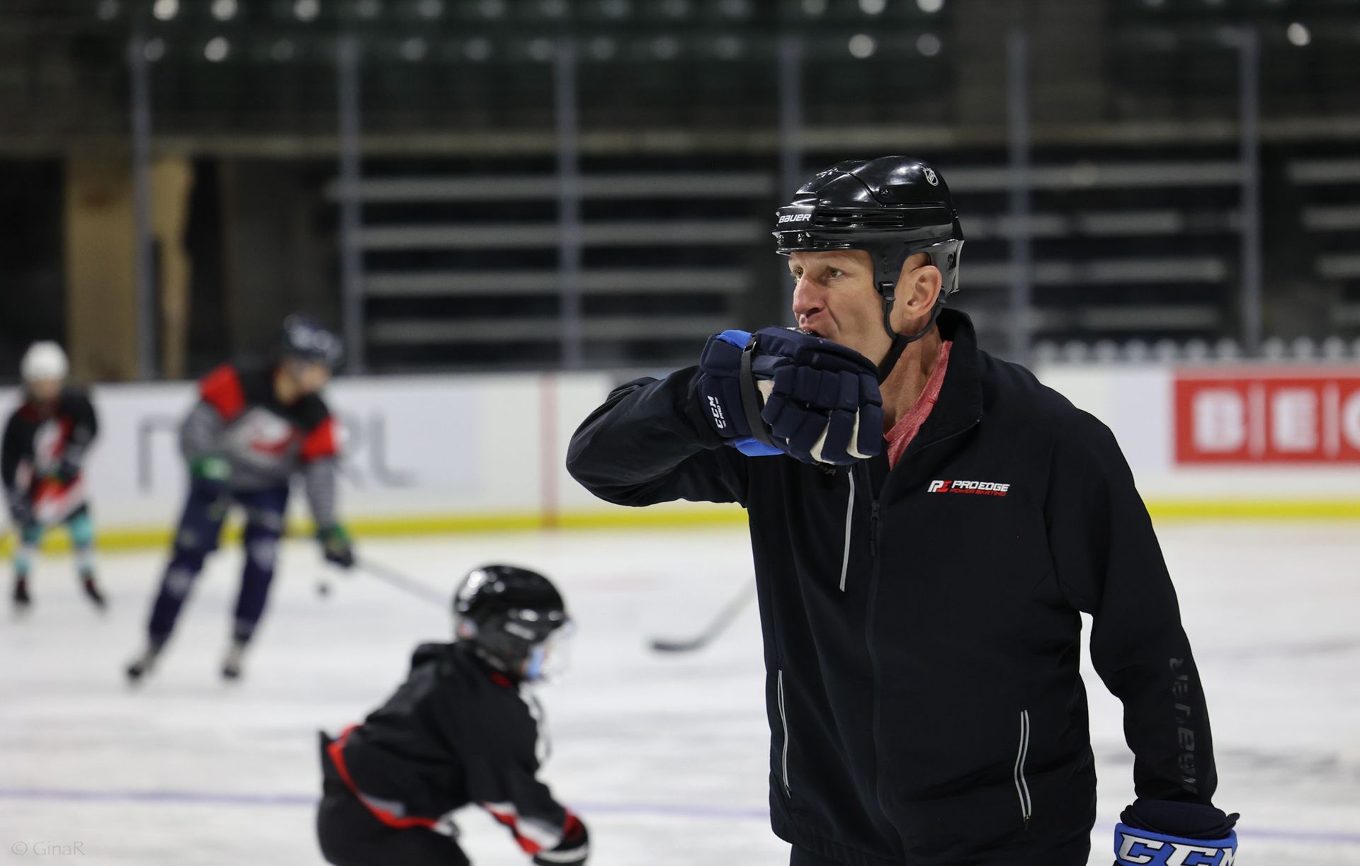 Hockey players skating on an ice rink, with one man in black foreground drinking from a bottle.
