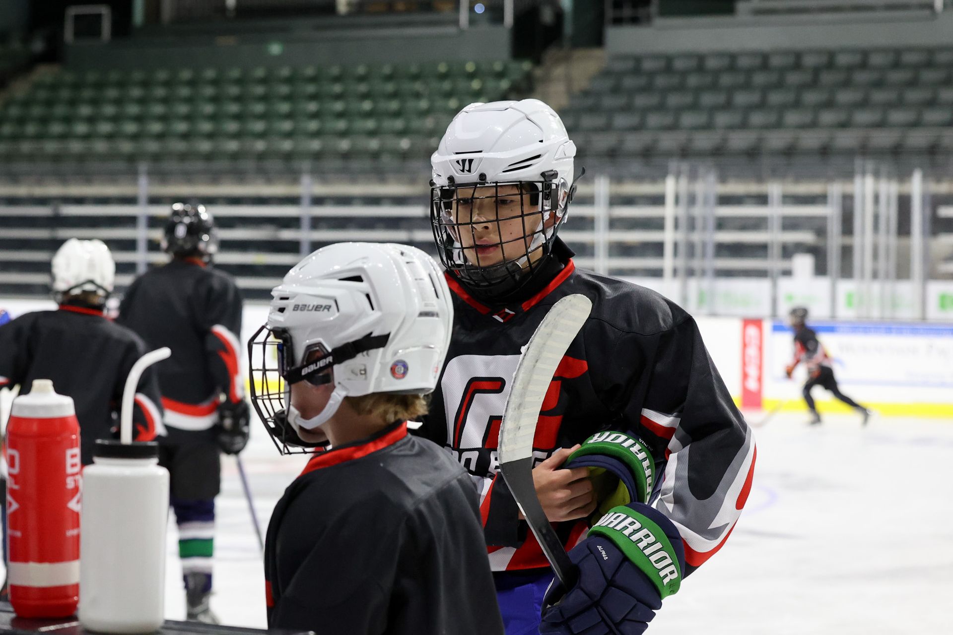 Two hockey players in helmets on an ice rink, one holding a colorful stick in the foreground