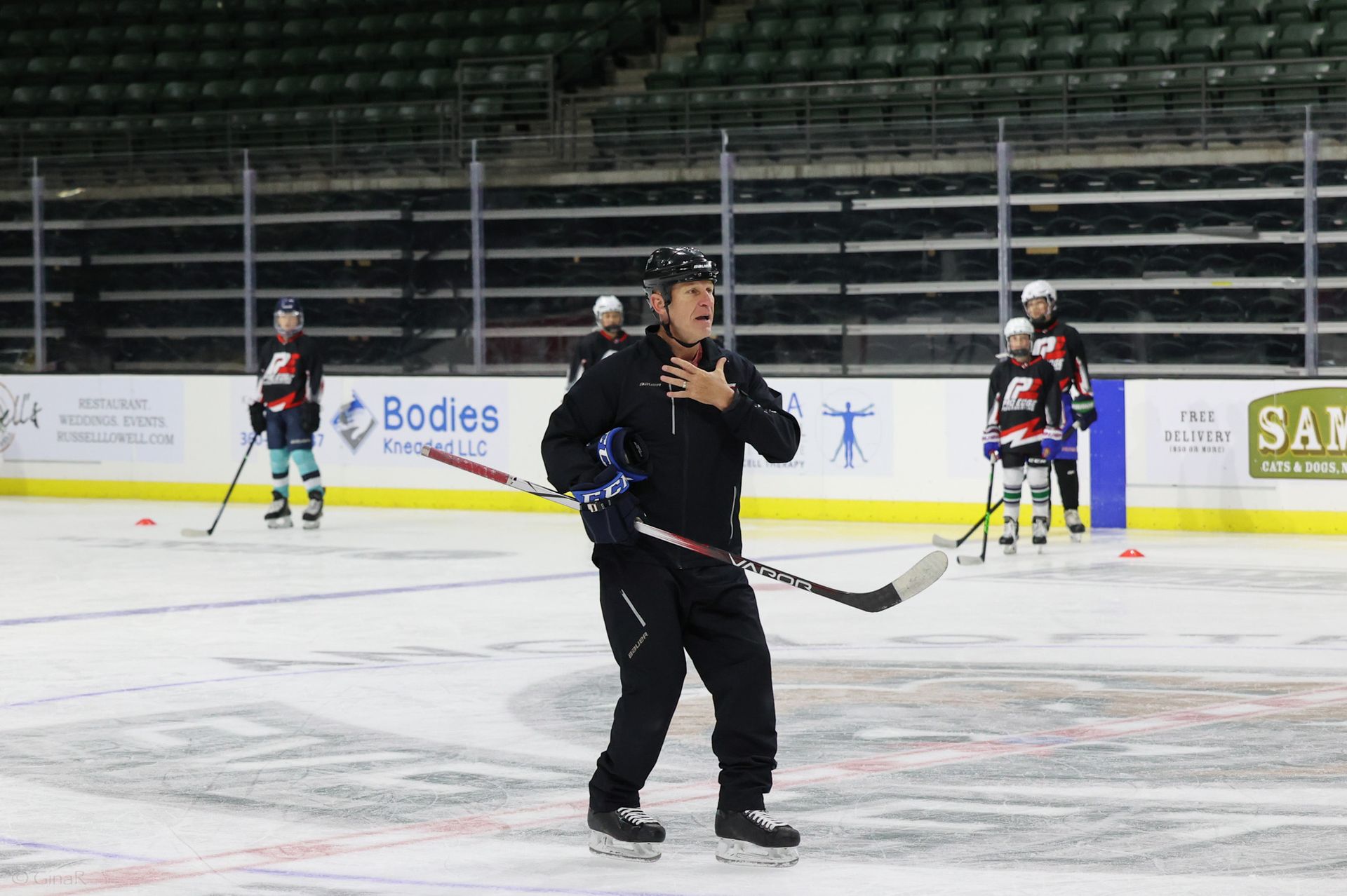 Hockey player in black skating on ice with teammates in the background during practice