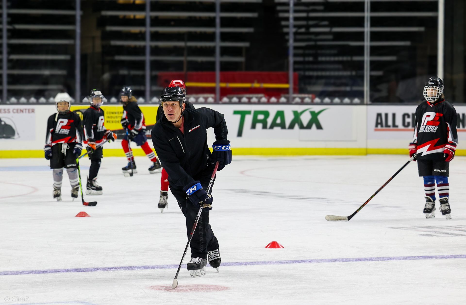 Hockey players practicing drills on an ice rink with cones and a coach in the foreground