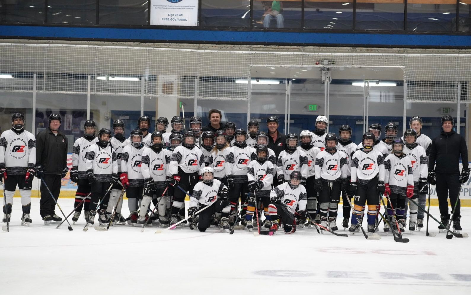 Youth hockey team posing on the ice in white jerseys, with coaches and a rink backdrop