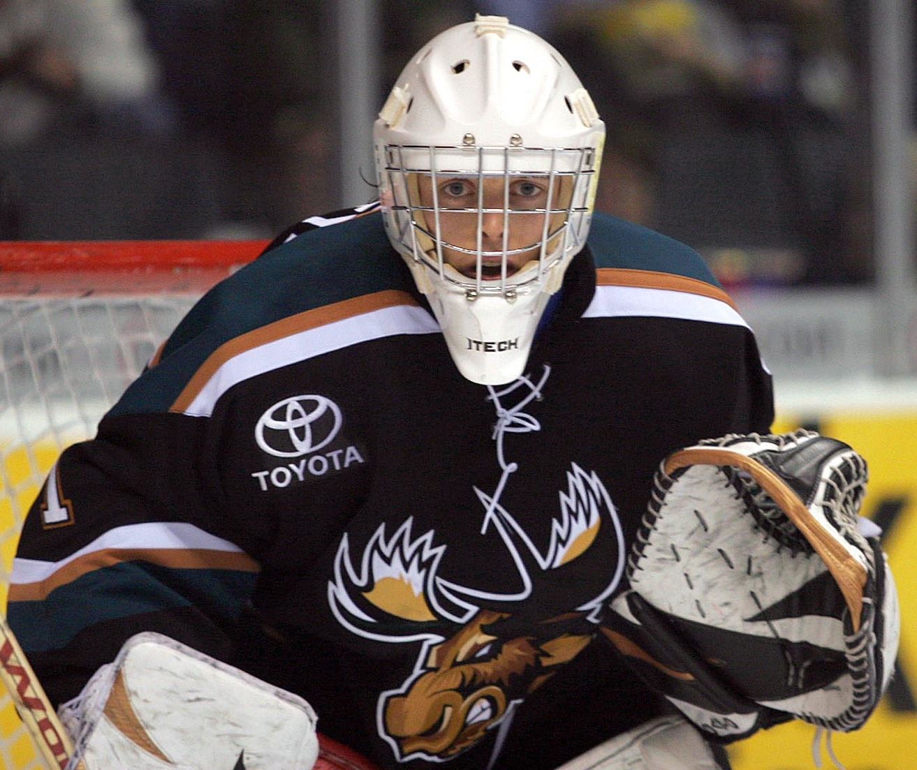 Ice hockey goalie in black jersey and white mask, crouched in front of the net
