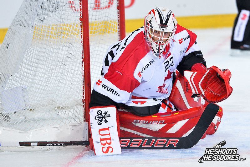 Ice hockey goalie in white and red gear crouches in front of the net, making a save.