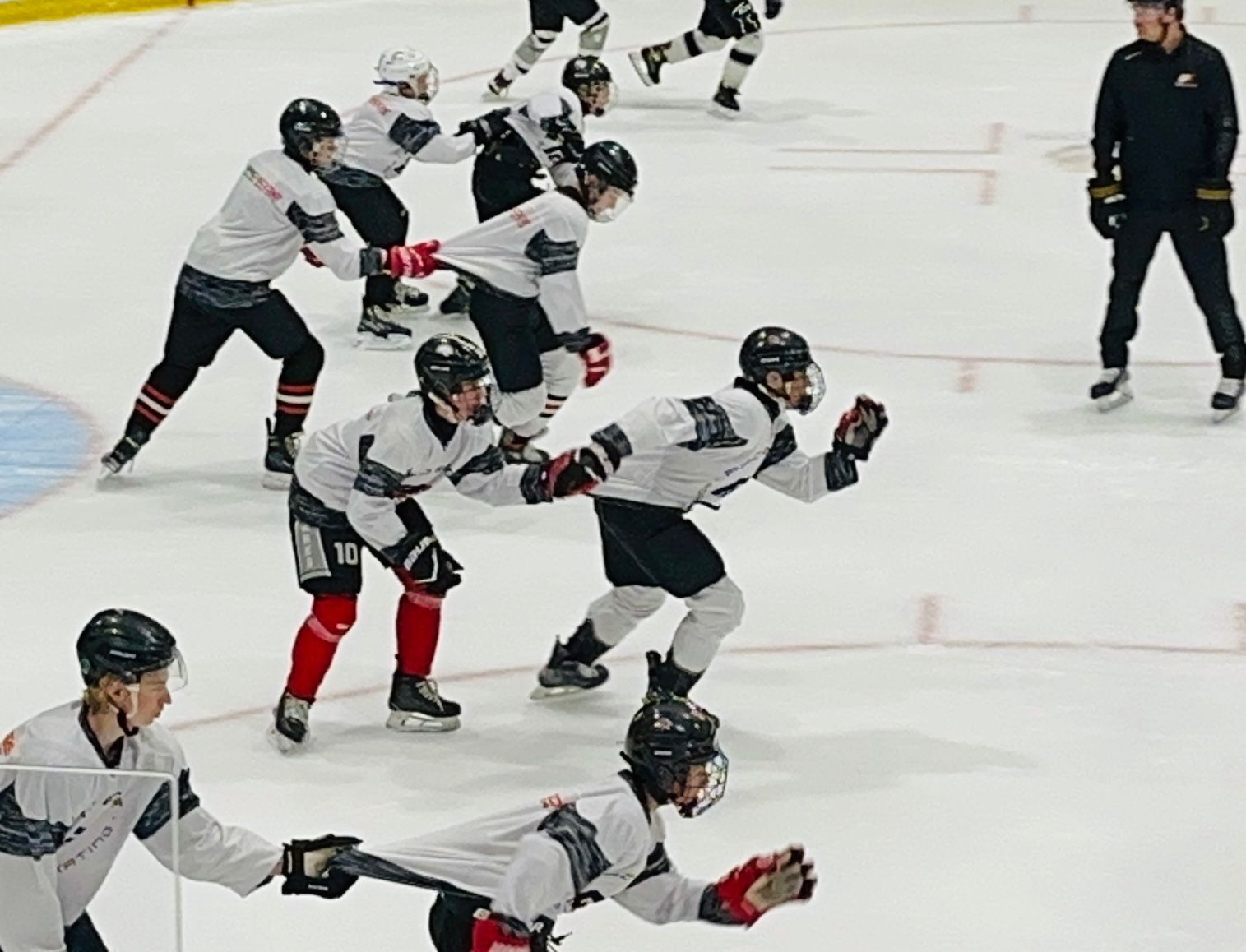 Ice hockey players in white jerseys skating on the rink during practice drills