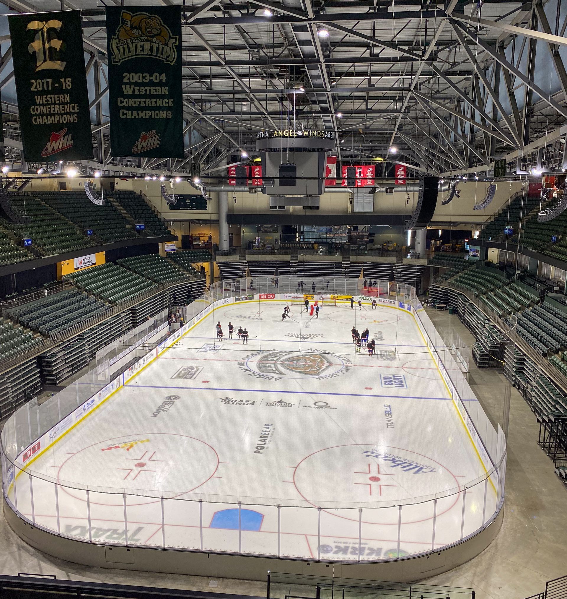 Indoor hockey arena with empty green seats and players on a covered ice rink preparing the surface