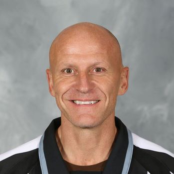 Smiling bald man in a black and white jacket against a gray studio background