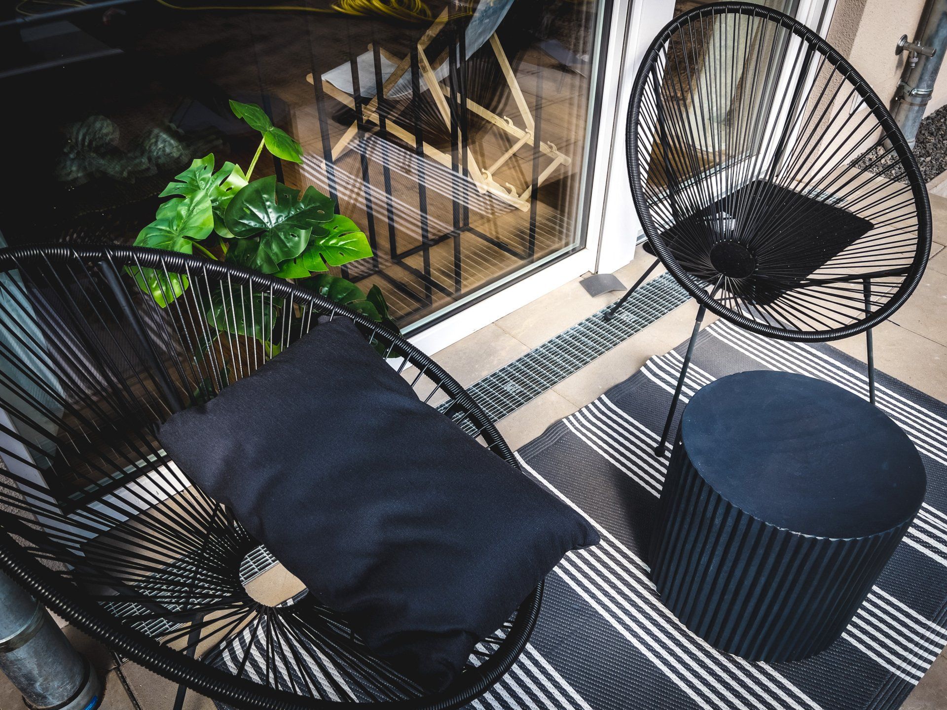 Auf einem Balkon stehen zwei schwarze Stühle und ein Ottomane.
