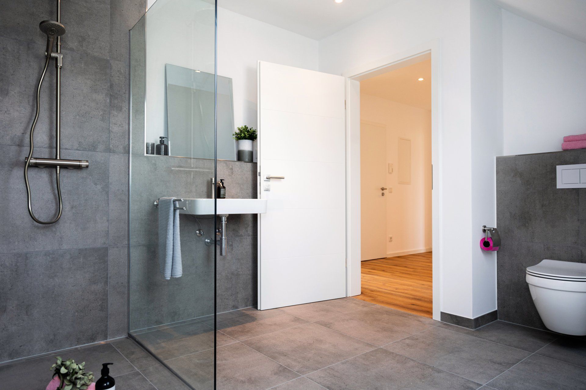 Ein Badezimmer mit ebenerdiger Dusche, Waschbecken, Toilette und Spiegel.