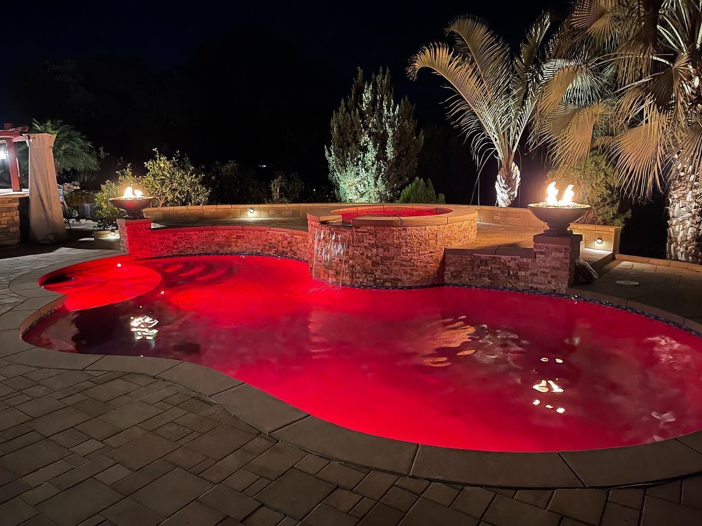 A large swimming pool is lit up at night with red lights.