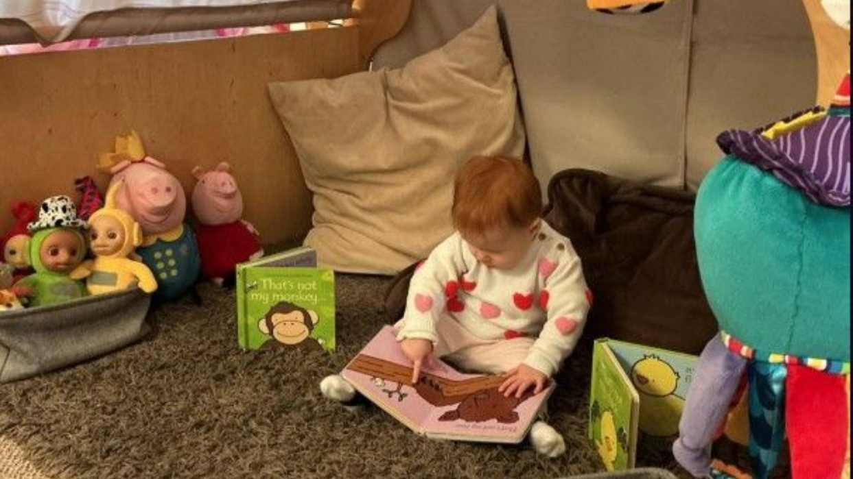 Baby exploring a book in the Bumblebees baby room at The Village Nursery, Bramcote