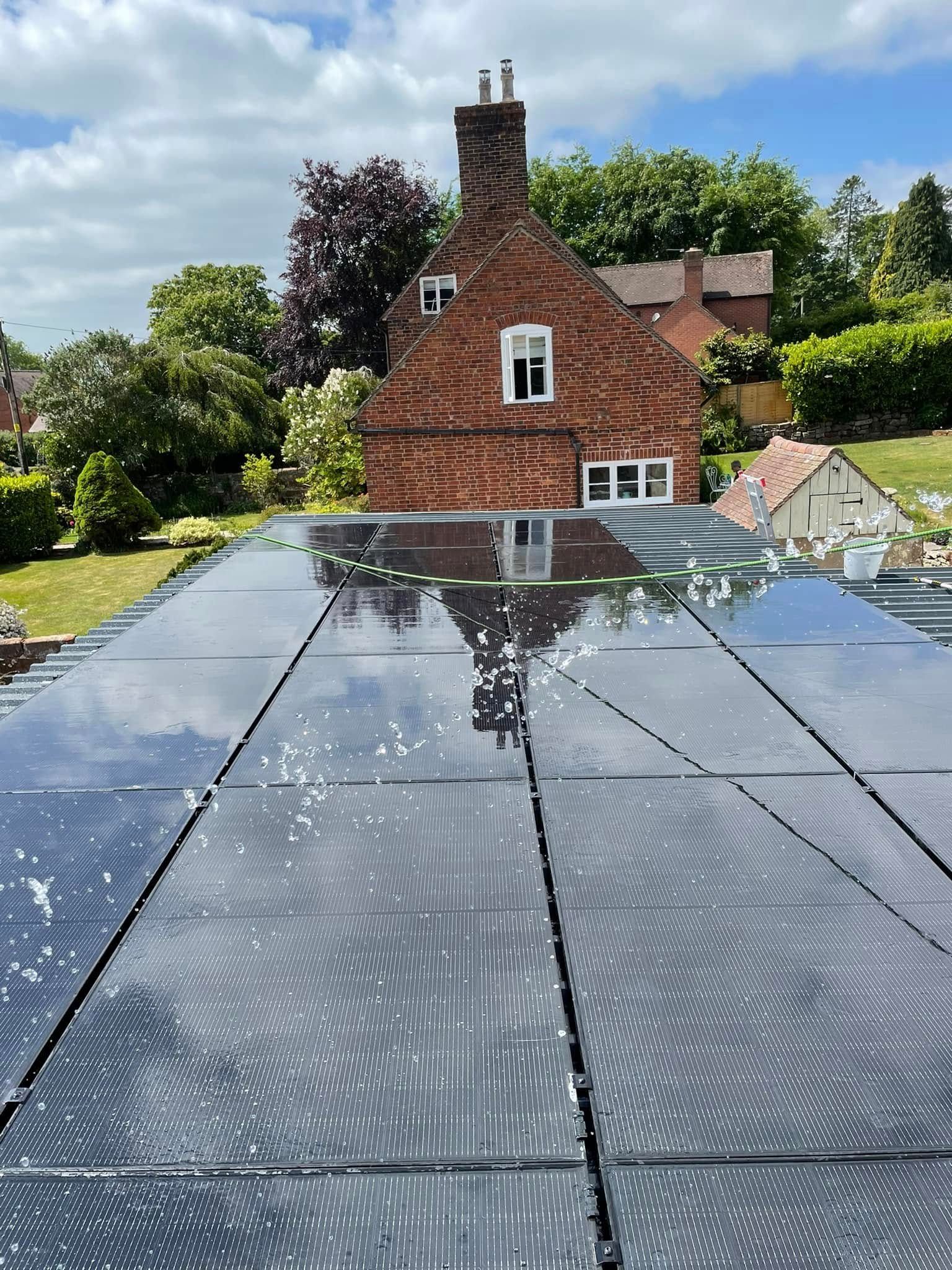 Solar panels on a roof reflecting a brick house and blue sky.