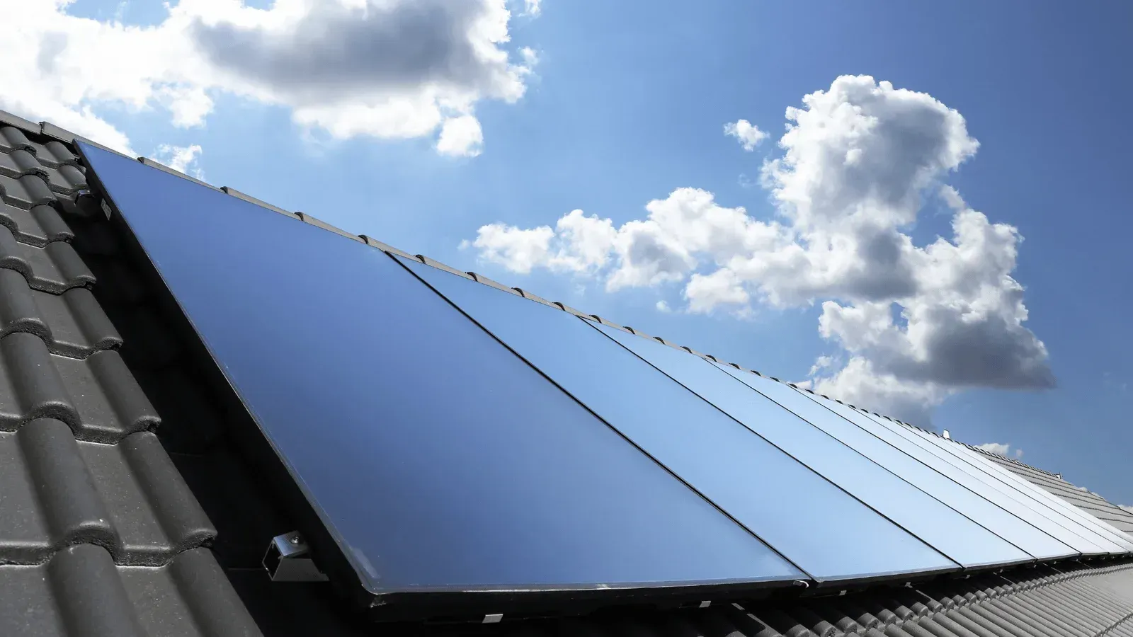 Solar panels on a roof against a blue sky with white clouds.