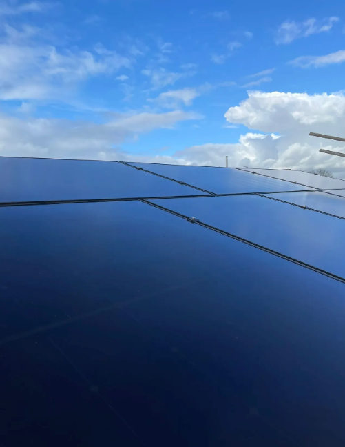 Solar panels on a roof against a blue sky with white clouds.