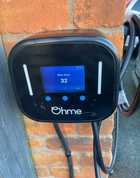 Black Ohme EV charger mounted on a brick wall, displaying