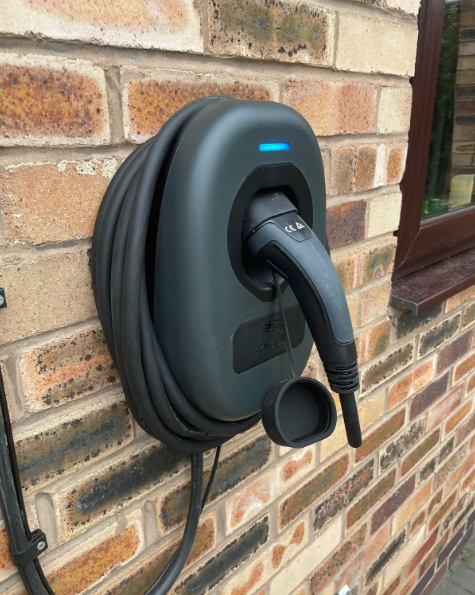 Black electric vehicle charger mounted on a brick wall with the cable coiled around it.