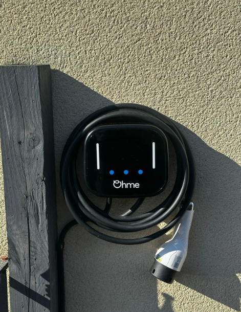 Black electric vehicle charger mounted on a wall with charging cable.