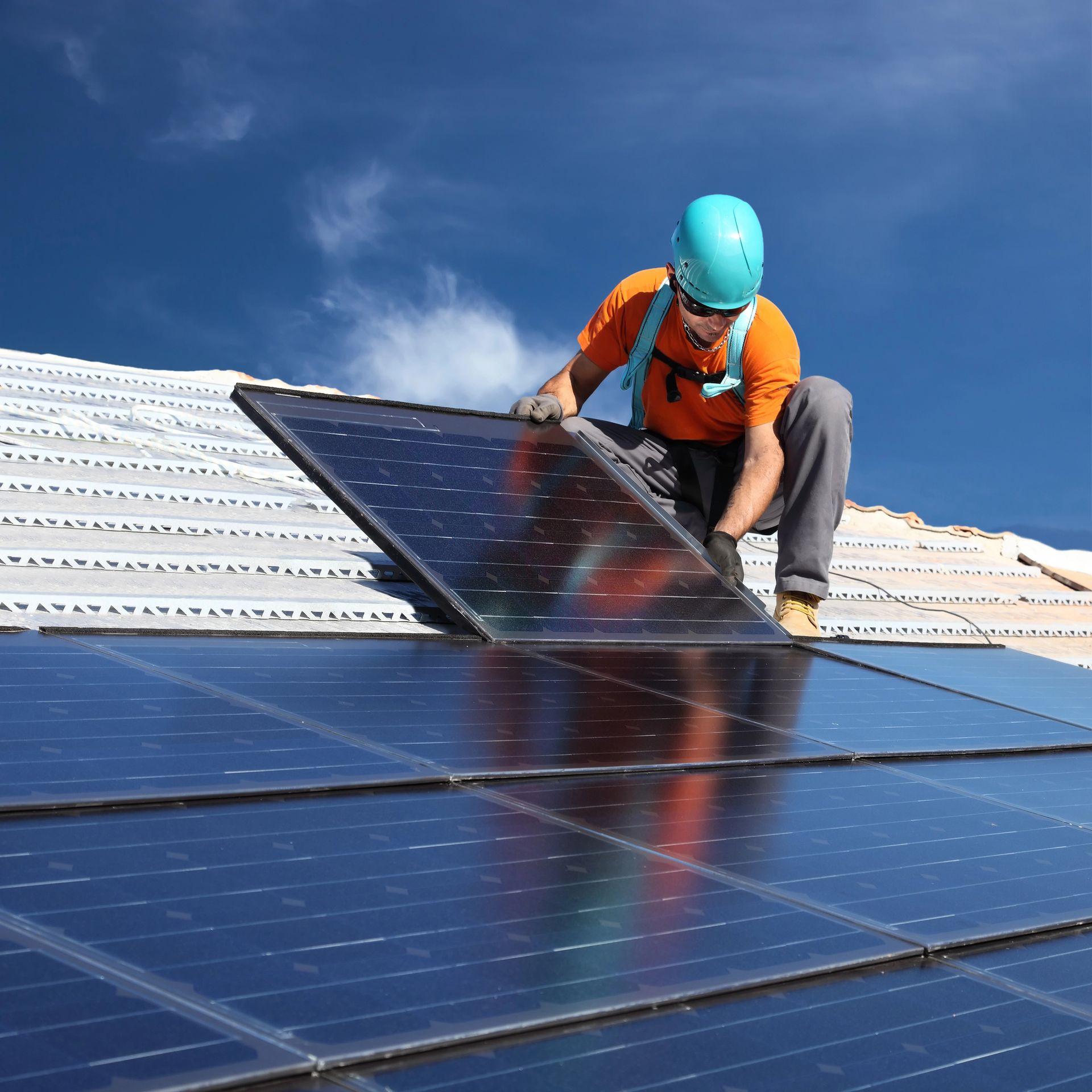 Rooftop solar panel installation: worker in safety gear places a panel on a roof under a blue sky.