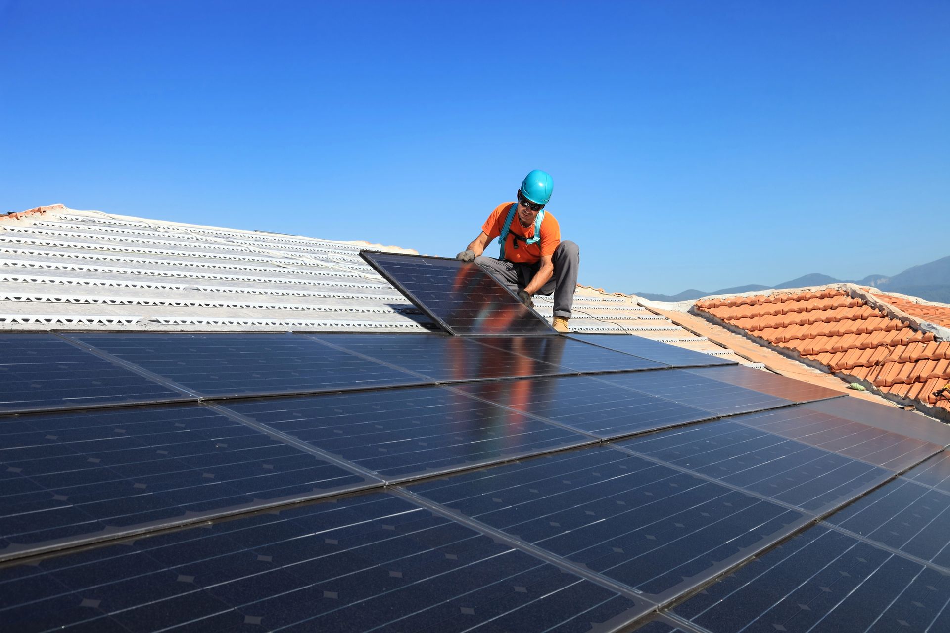A man is installing solar panels on the roof of a house.
