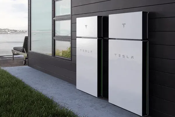 Two Tesla Powerwall batteries outside a modern house with a green lawn and view.