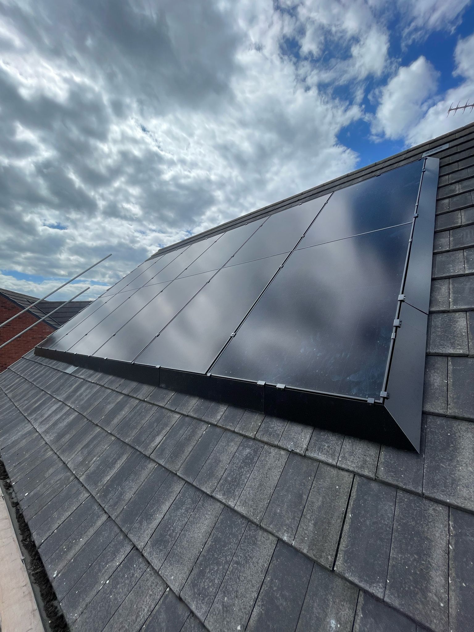 Solar panels installed on a dark gray shingled roof, against a cloudy sky.