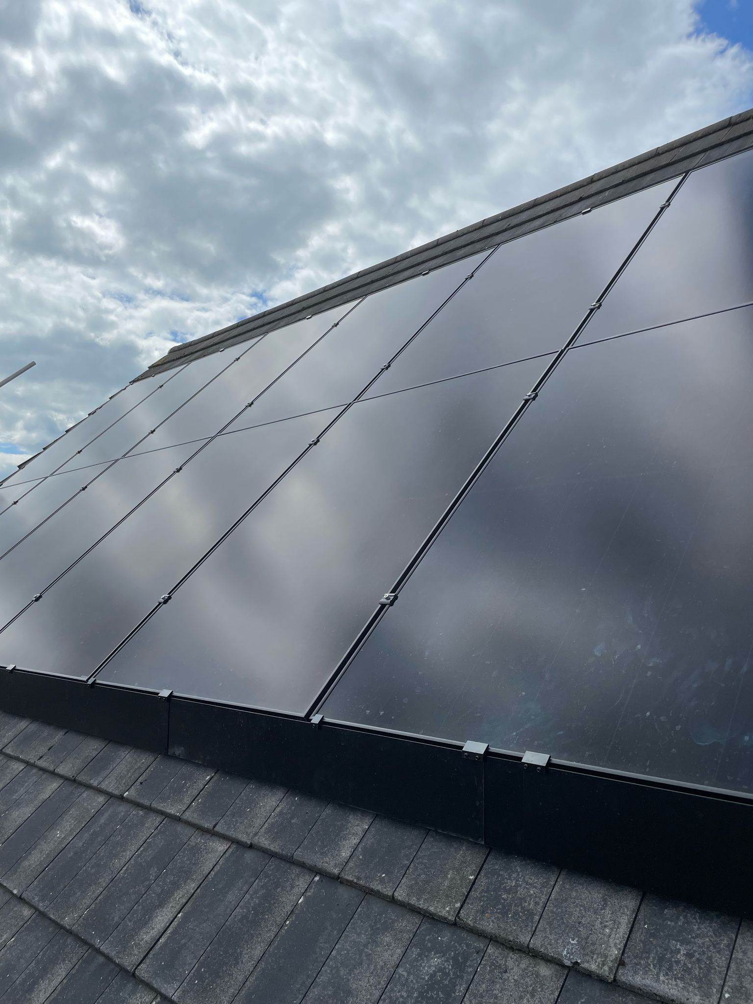 Solar panels on a dark-shingled roof against a cloudy sky.