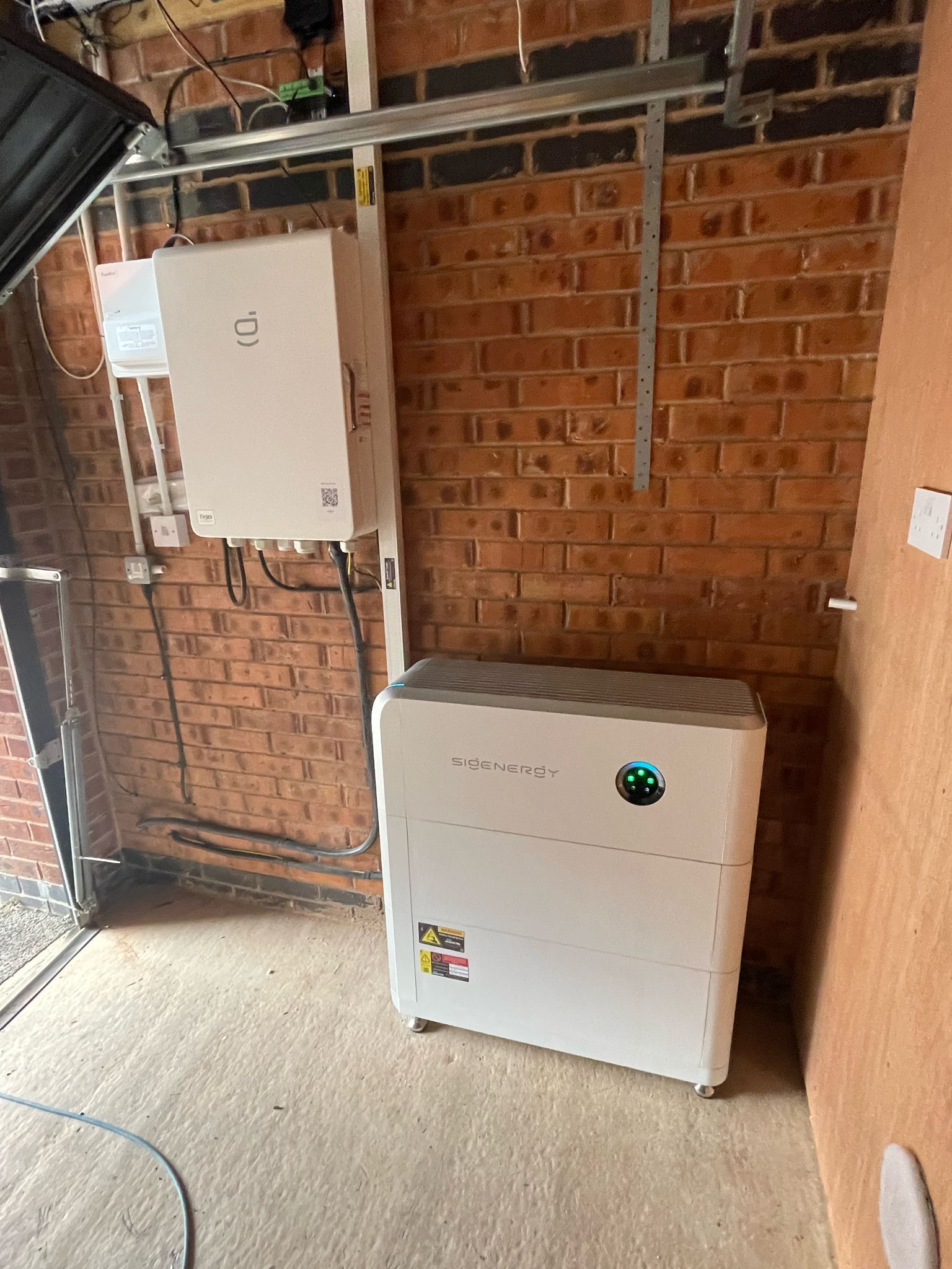 White solar battery system components mounted on a brick wall in a garage.