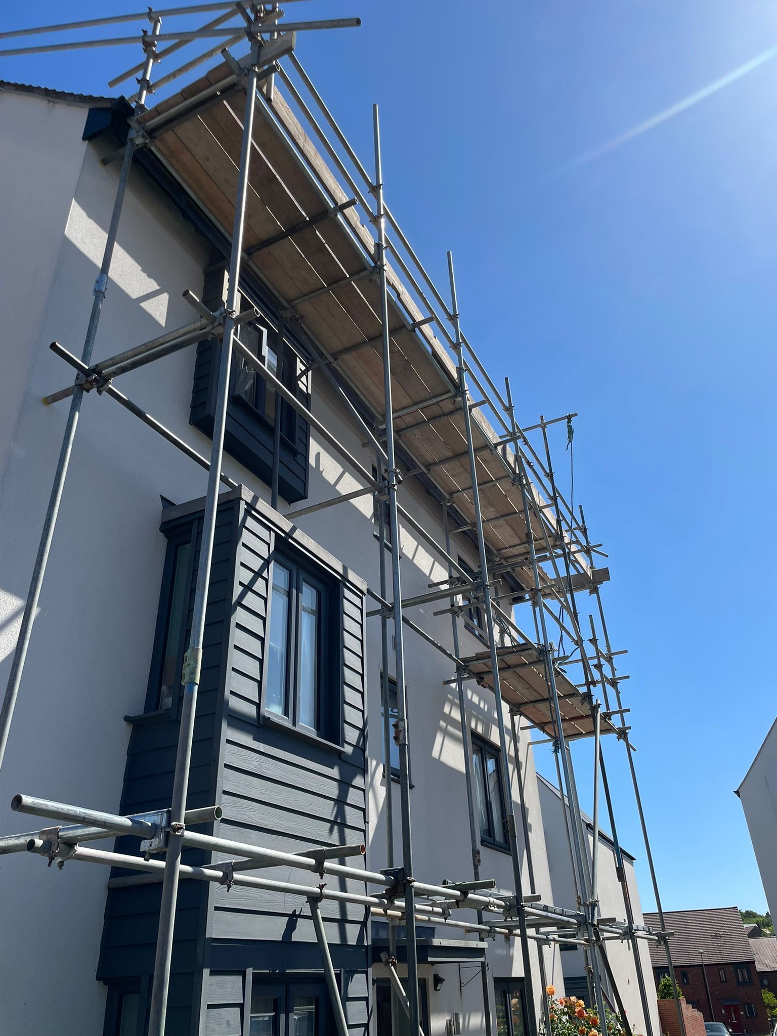 Scaffolding on a two-story house with white walls and gray trim under a blue sky.