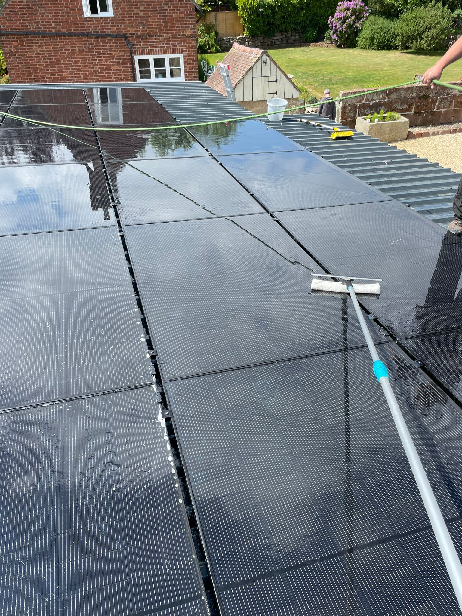 Person cleaning solar panels on a rooftop with a long-handled squeegee.